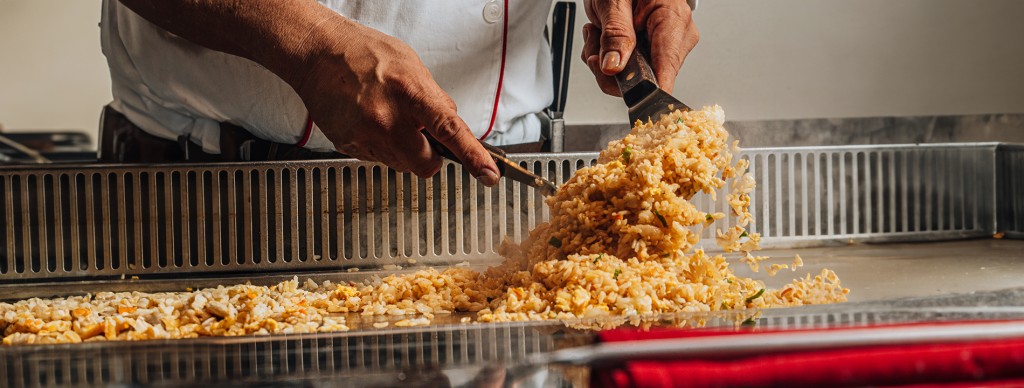 A hibachi chef prepares fried rice on a teppanyaki grill, tossing the rice with a spatula.